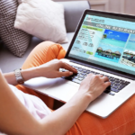 Relaxing on white couch, booking online trip reservation on laptop.