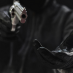 Dark figure pointing handgun with outstretched hand, creating tense atmosphere.