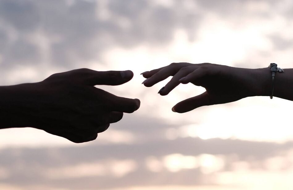 Reaching hands symbolize human connection and diversity against a tranquil dawn sky.