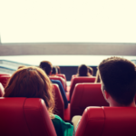 Empty cinema theater with red seats and blank screen, creating a cozy and cinematic atmosphere.