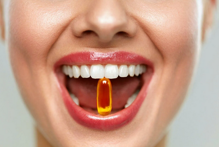 Smiling person with golden capsule between teeth, promoting beauty and wellness.