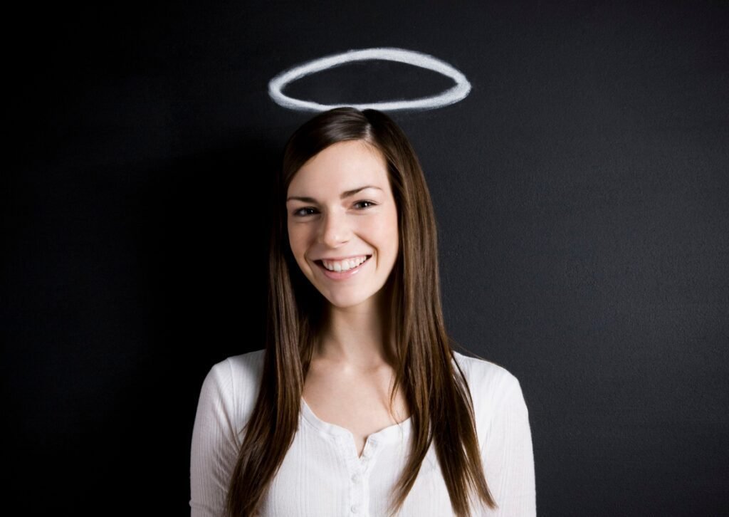 A smiling woman with long brown hair, wearing a white blouse, positioned in front of a black background with a chalk-drawn halo above her head.