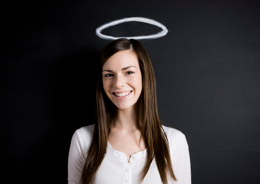 A smiling woman with long brown hair, wearing a white blouse, positioned in front of a black background with a chalk-drawn halo above her head.