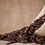 Rustic coffee beans spill from burlap sack onto tabletop, showcasing warm tones and textures.
