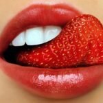 Sensual red lips holding ripe strawberry, creating vibrant color contrast.