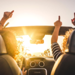 Joyful road trip in convertible car at golden hour, passing palm trees on coast.