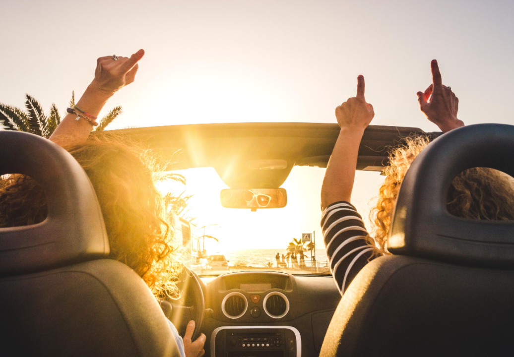 Joyful road trip in convertible car at golden hour, passing palm trees on coast.