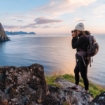 Tranquil coastal hiker with binoculars overlooking serene ocean on rocky cliff at sunset.