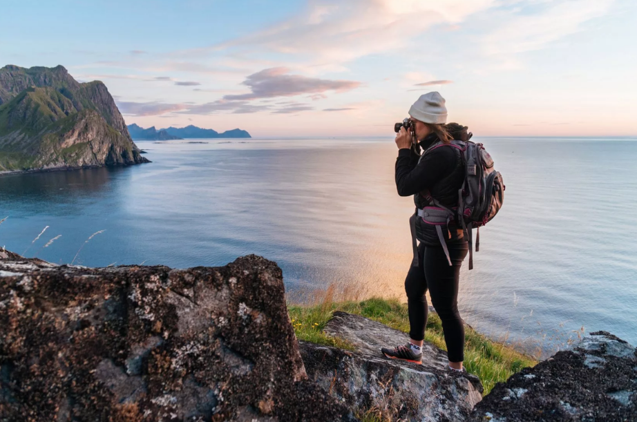 Tranquil coastal hiker with binoculars overlooking serene ocean on rocky cliff at sunset.