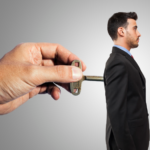 Surreal image of hand inserting key into businessmans back, symbolizing control and influence.