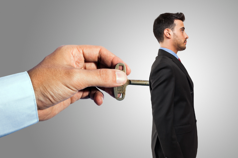 Surreal image of hand inserting key into businessmans back, symbolizing control and influence.