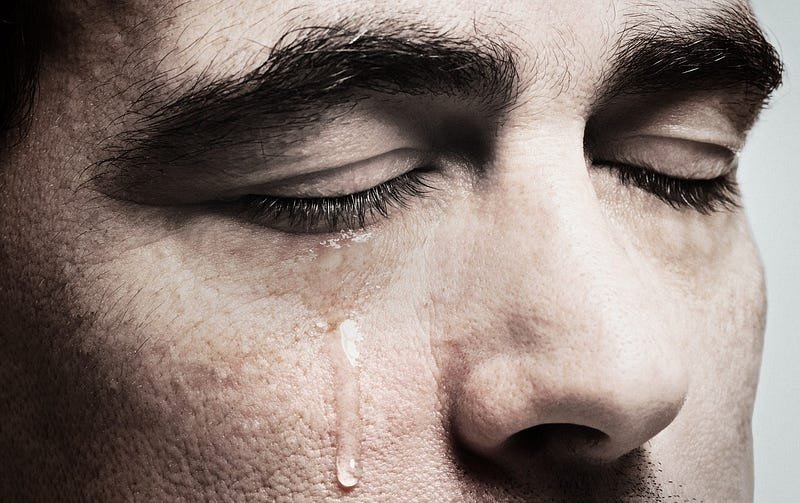 Close-up of a man's face with his eyes closed and a tear rolling down his cheek.