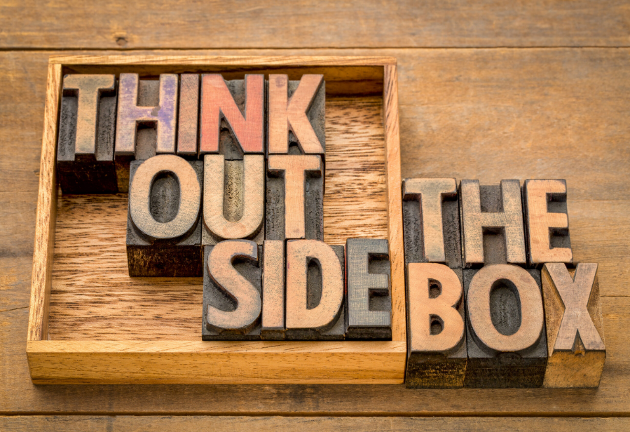 Letterpress wooden blocks spelling 'THINK OUTSIDE THE BOX' in a wooden box on a wooden surface.