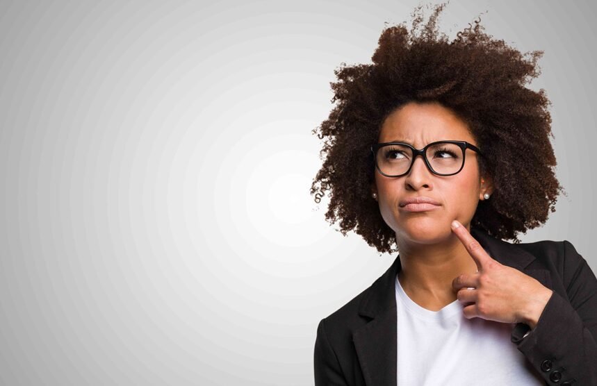 Professional woman in afro hairstyle and black blazer gazes thoughtfully against gray backdrop.