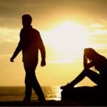 Silhouetted figures at ocean sunset, one walking, one seated in contemplation.