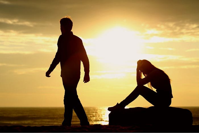 Silhouetted figures at ocean sunset, one walking, one seated in contemplation.