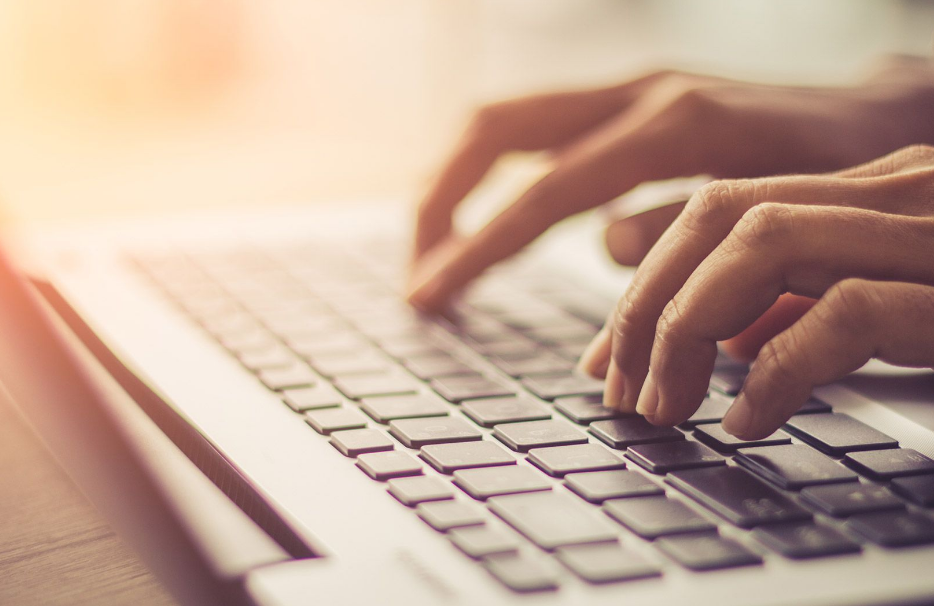 Close-up of a person's hands typing on a laptop keyboard with a warm light in the background.