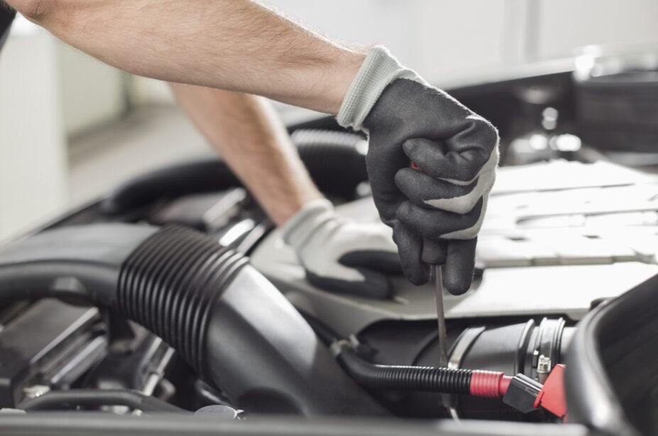 A mechanic's hands wearing gloves, using a screwdriver on an engine component inside a vehicle's bonnet.