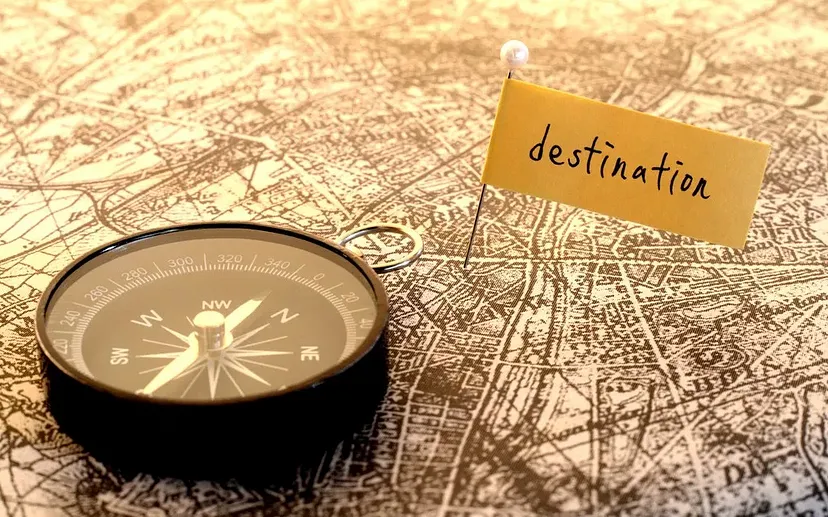 A compass on top of a vintage map with a pin and a tag with the word "destination" written on it.