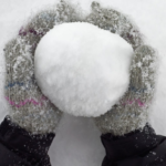 Colorful gloves holding freshly made snowball in snowy landscape, capturing winter joy.