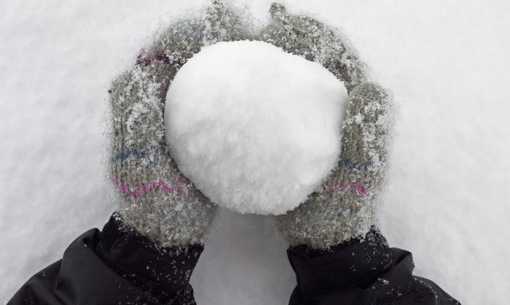 Colorful gloves holding freshly made snowball in snowy landscape, capturing winter joy.