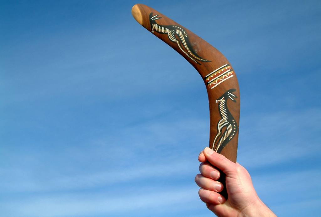 A hand holding an Aboriginal Australian style decorated boomerang against a clear blue sky.