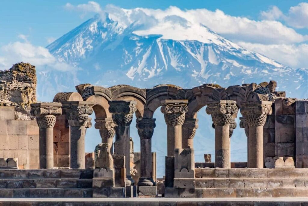 Ancient stone ruins with intricately carved arches in the foreground, with Mount Ararat in the background under a clear blue sky.