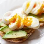 Elegant avocado toast with soft-boiled egg, spices, on white plate.