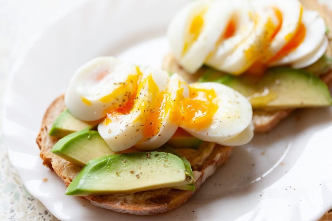 Elegant avocado toast with soft-boiled egg, spices, on white plate.