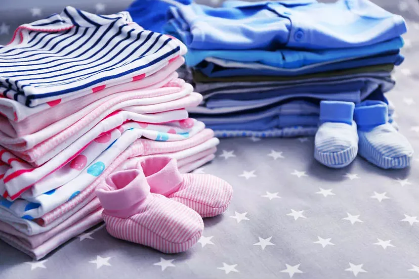 Piles of neatly folded baby clothes and two pairs of small baby booties on a star-patterned fabric surface.