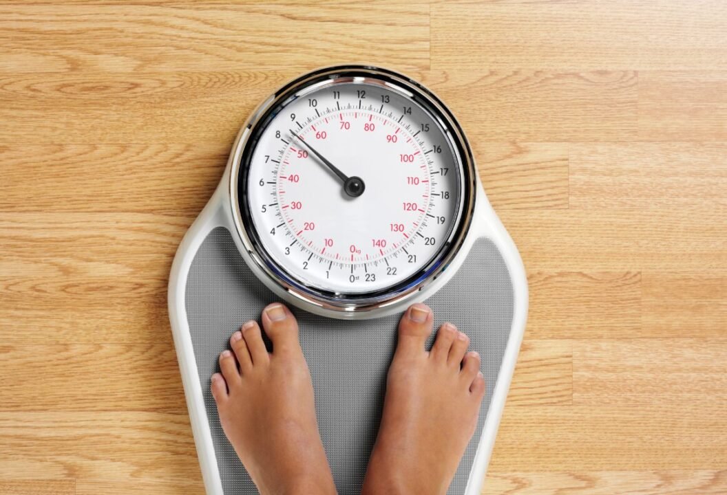 Person standing on bathroom scale for weight measurement on wooden floor.
