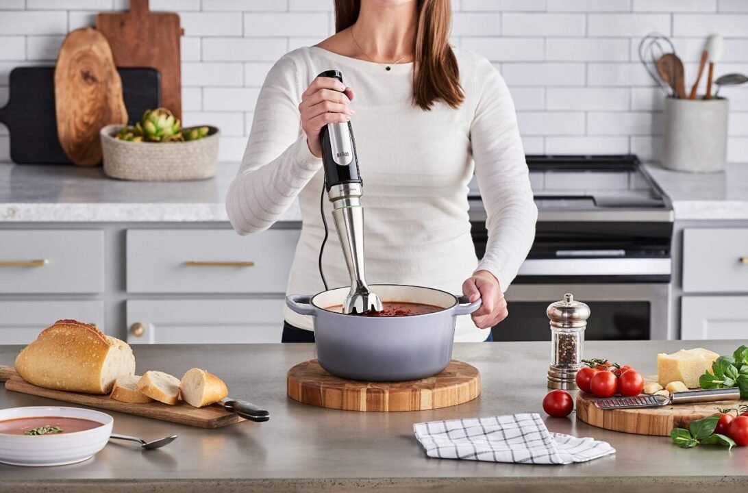 Woman using an immersion blender to puree tomato sauce in a pot in a modern kitchen.