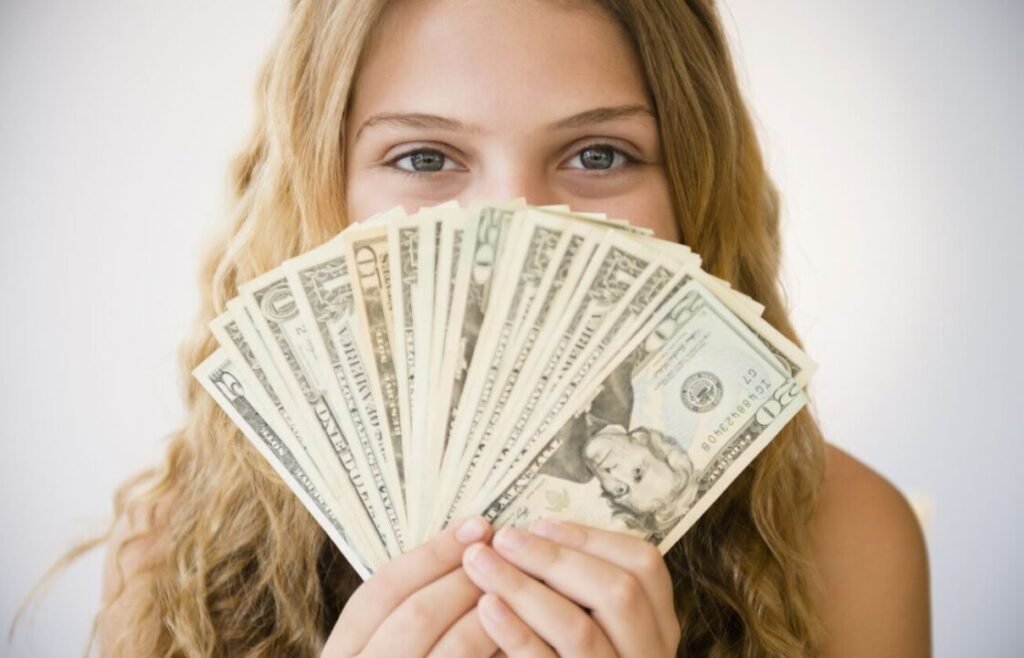 Excited woman holding fan of $20 bills, eyes sparkling with joy.
