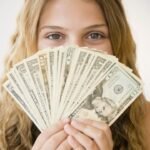 Excited woman holding fan of $20 bills, eyes sparkling with joy.