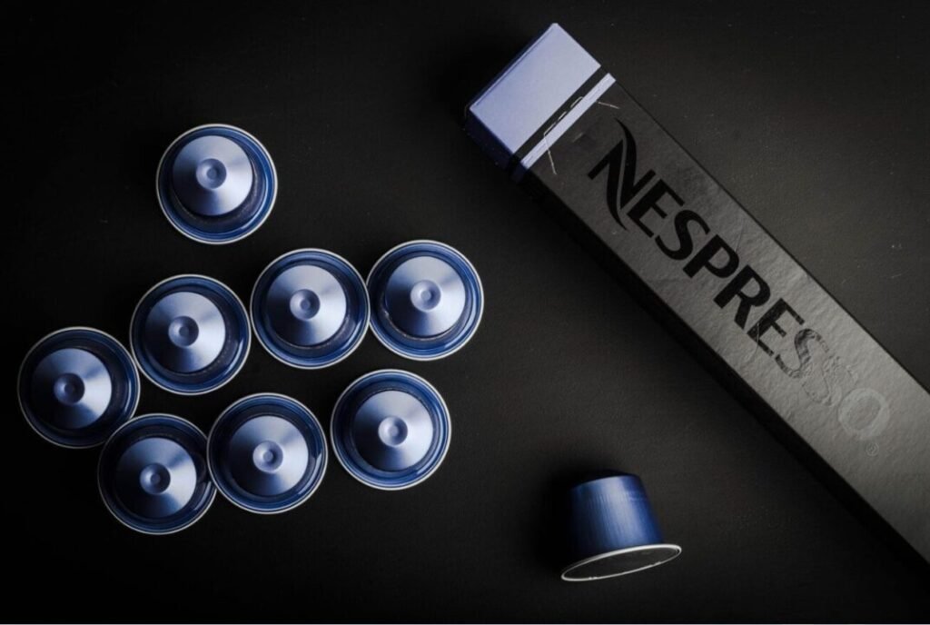 A collection of blue coffee capsules on a black surface alongside a black Nespresso-branded box.