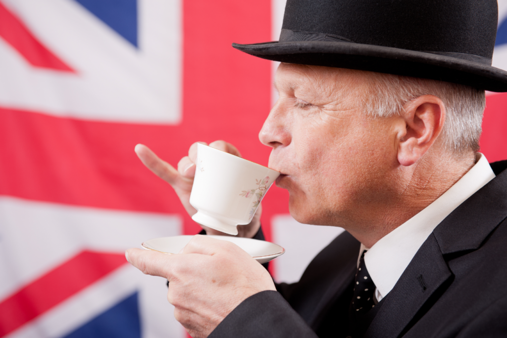 A man in a bowler hat and suit sipping tea from a fine china cup with the UK flag in the background.