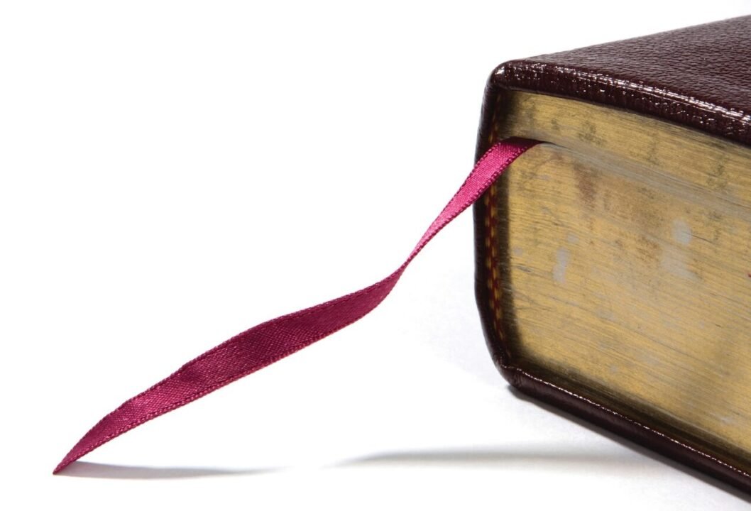 A close-up of a brown leather-bound book with a red ribbon bookmark sticking out.