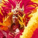 Person in vibrant red and yellow carnival costume with feather headdress dancing joyfully.