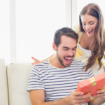 Happy couple surprised with gift on white couch in bright room.