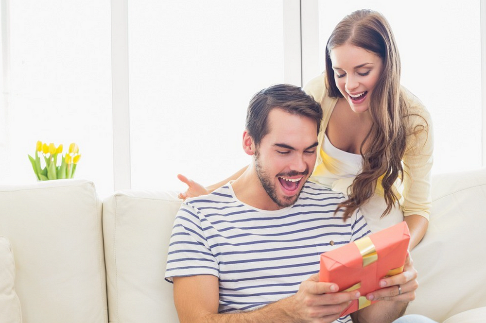 Happy couple surprised with gift on white couch in bright room.