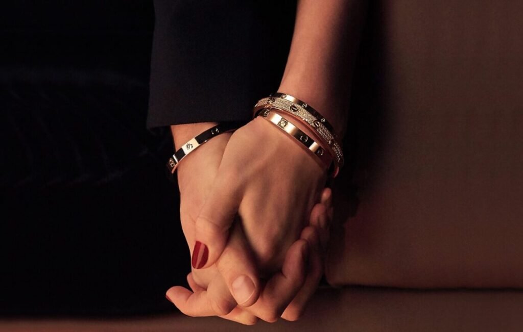 Close-up of two hands clasped together, one wearing several luxury bracelets, against a dark background.