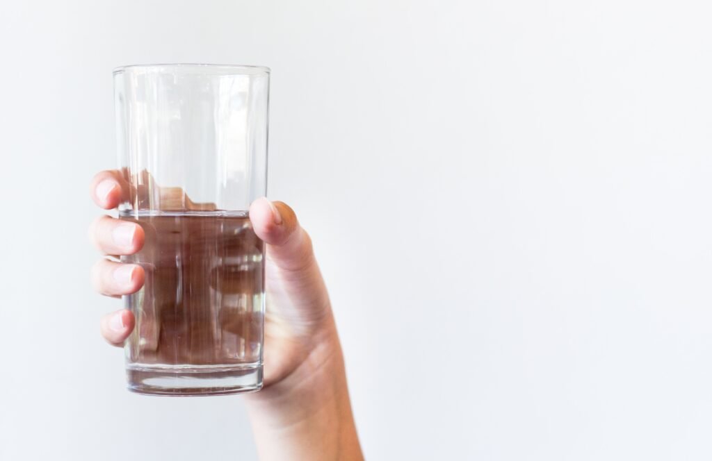 A human hand holding a half-full clear glass of water against a white background.