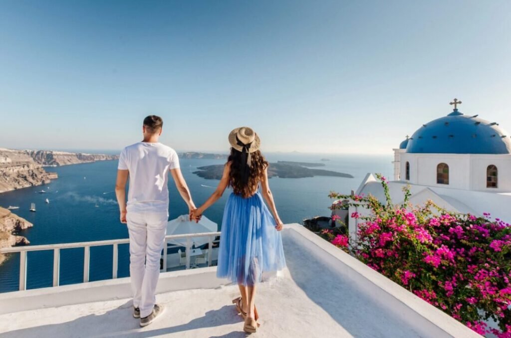 Romantic couple holding hands on terrace overlooking blue-domed church and sea in Santorini.