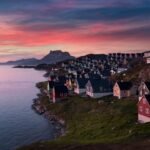 Tranquil coastal village at sunset with mountain backdrop and colorful houses by the sea.