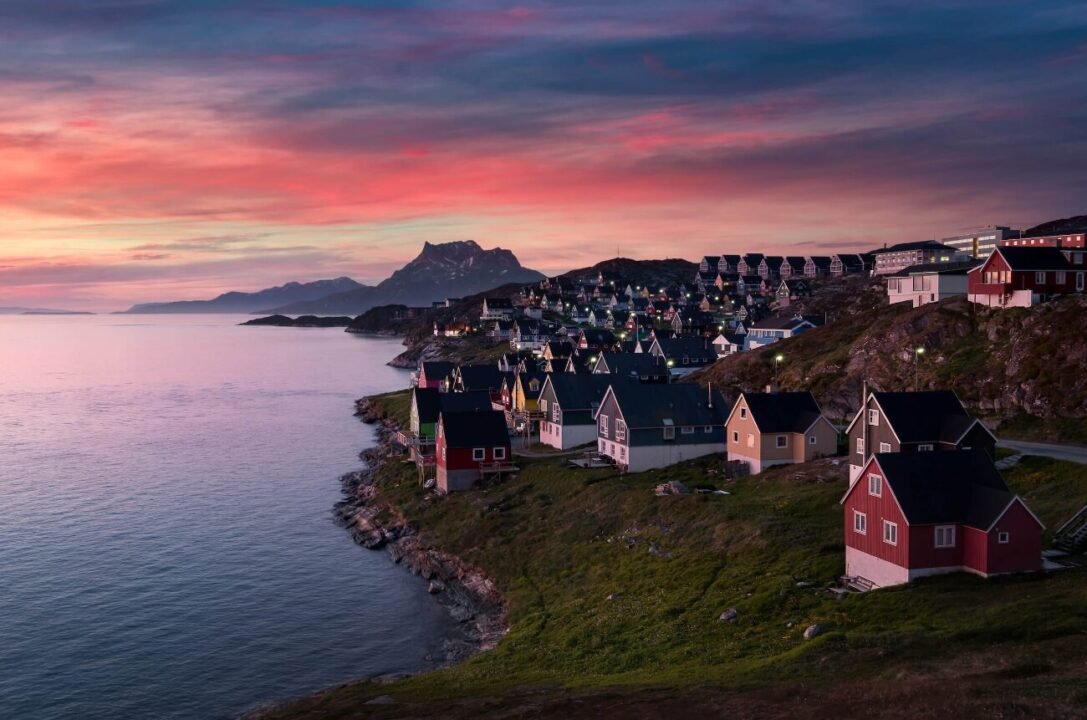 Tranquil coastal village at sunset with mountain backdrop and colorful houses by the sea.