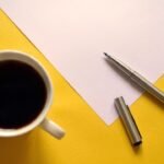 Coffee, pen, paper: a creative moment on vibrant yellow background.