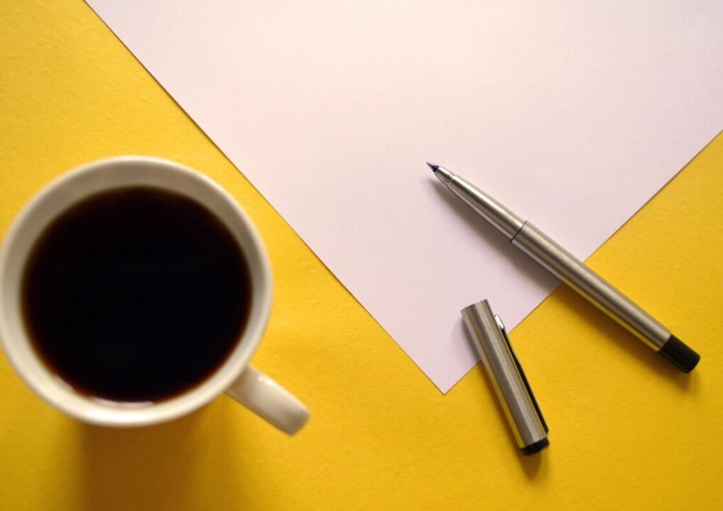 Coffee, pen, paper: a creative moment on vibrant yellow background.