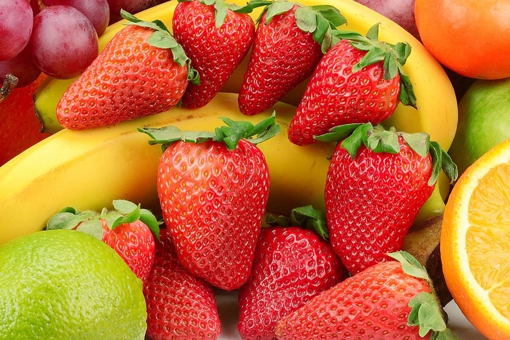 Fresh and vibrant fruit arrangement with strawberries, bananas, oranges, grapes, and lime.