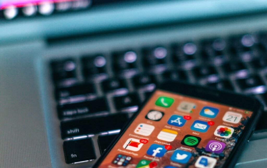 Smartphone with various app icons displayed resting on a laptop keyboard with blurred lights in background.