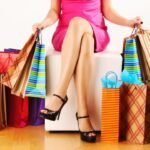 Woman in pink dress surrounded by colorful shopping bags after successful spree in cozy setting.